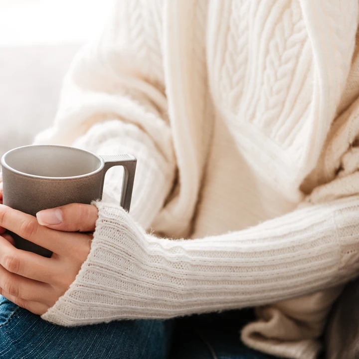 Kvinna med kaffekopp sitter i en soffa.