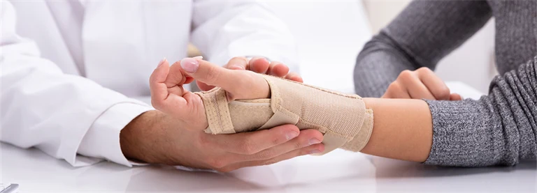 En kvinna får sin handled inlindad i bandage av en doktor.