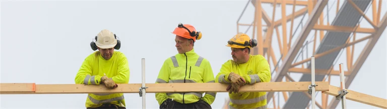 Tre byggjobbare står lutade mot ett räcke och samtalar