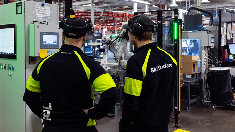 Två anställda på ROL Group tittar ut över fabriksmiljön. ROL Group har sökt och fått stöd för arbetsmiljöutbildning.