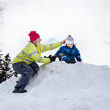 Försskolepedagog hjälper litet barn uppe på en snöhög