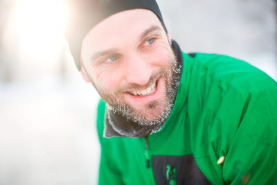 Man med snö i skägget, mössa och grön vinterjacka