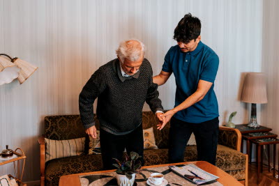 Hemtjänst hjälper upp en brukare från soffan