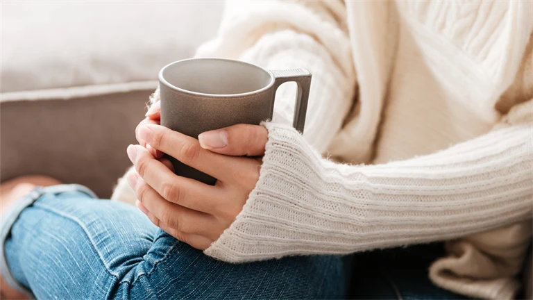 Kvinna med kaffekopp sitter i en soffa.