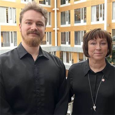 Jonathan Källbäcker och Åsa Cajander, forskare, står i Afa Försäkrings lokaler och ler mot kameran. De har båda svarta kläder.