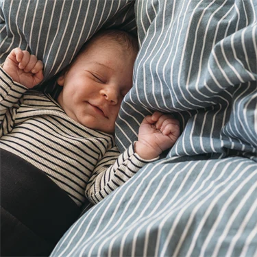 Bebis ligger och sover på randigt, fluffigt täcke.