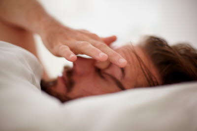 Man ligger i sängen med handen över ansiktet