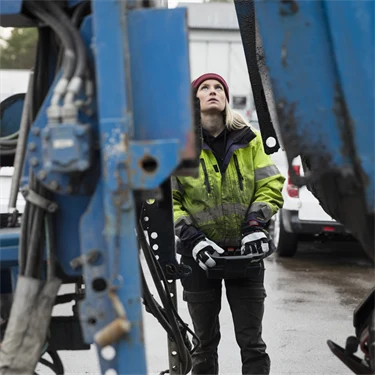 Kvinna i arbetskläder manövrerar stor maskin eller fordon med joystick eller liknande, 
