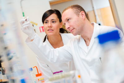 Två forskare i vita rockar tittar på ett provrör.