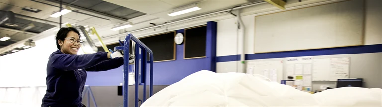 Duang-Jan Larsson arbetar i lagsalen på Voith, med att manuellt dra en vagn med vävar som man manuellt flyttar till nästa avdelning.