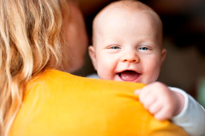 Glad bebis skrattar över mammas axel
