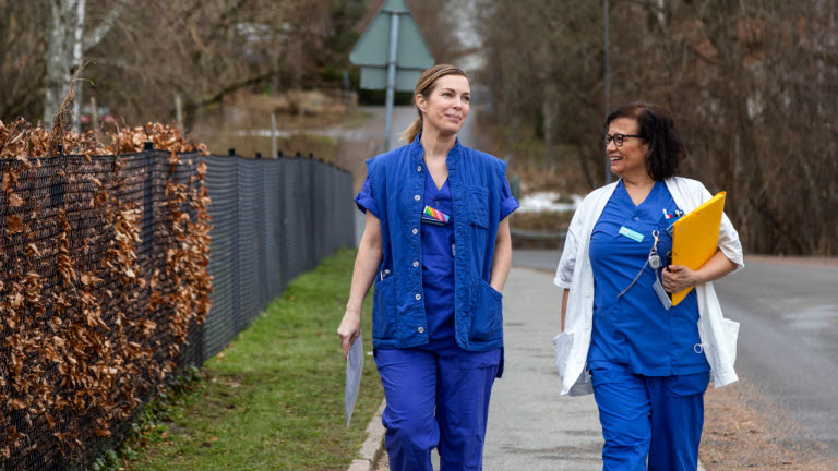 Två leende sjuksköterskor promenerar utomhus