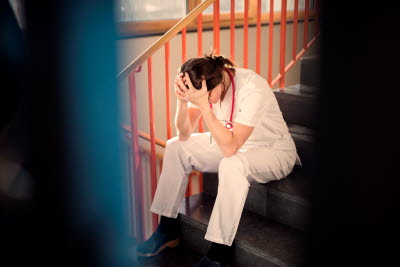 Trött sjukvårdare vilar huvudet i händerna