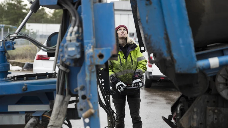 Kvinna i arbetskläder manövrerar stor maskin eller fordon med joystick eller liknande,