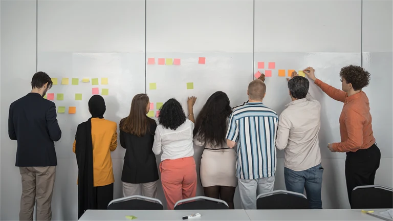 Medarbetare arbetar med post-it-lappar på stor tavla, planering, idéarbete eller visualisering