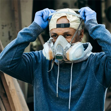 Man med skyddshandskar och bakåtvänd keps sätter på sig en skyddsmask
