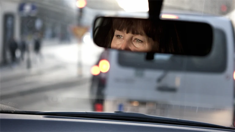 En person som kör bil och som tittar i backspegeln.
