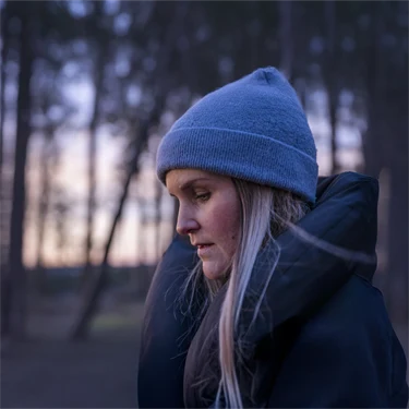 Kvinna med mössa på skogspromenad i skymning eller gryning