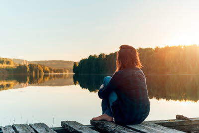 Kvinna på brygga ser ut över vattnet i skymningen