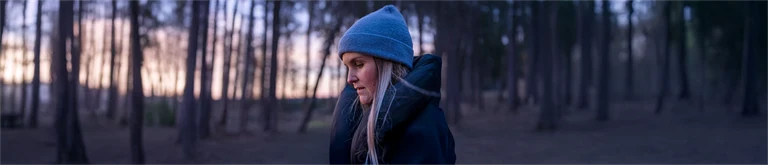 Kvinna med mössa på skogspromenad i skymning eller gryning