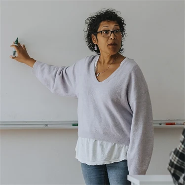 Lärare står och pekar på whiteboard i klassrum med elever i övre tonåren