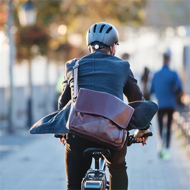 Man i kavaj cyklar med datorväska hängandes över ryggen