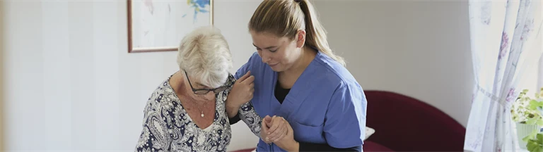 kvinnlig vårdpersonal hjälper äldre kvinna att resa sig från sin säng. 
