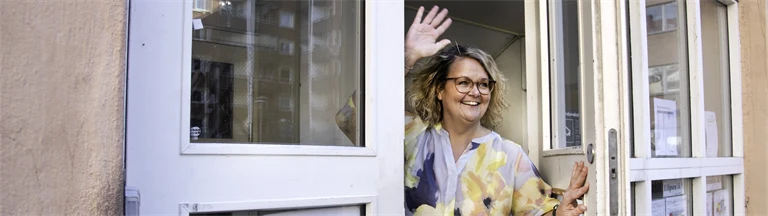 Pernilla Olsson vinkar genom en öppen dörr