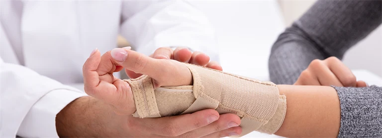 En kvinna får sin handled inlindad i bandage av en doktor.